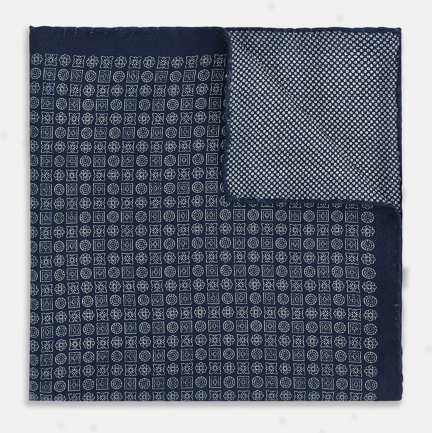 View 3 of product The Rosette Navy Pocket Square in Silk by Turnbull & Asser UK is a square, navy blue accessory featuring a small geometric pattern. Shown laid flat with one corner folded, it reveals a contrasting, finer motif on the reverse side. This elegant double-sided design offers versatile styling options for any occasion.