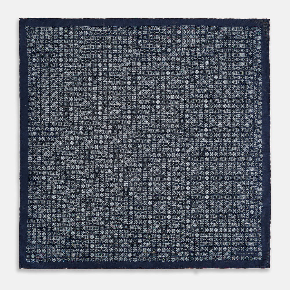 The Rosette Navy Pocket Square in Silk by Turnbull & Asser UK is a square, navy blue accessory featuring a small geometric pattern. Shown laid flat with one corner folded, it reveals a contrasting, finer motif on the reverse side. This elegant double-sided design offers versatile styling options for any occasion.