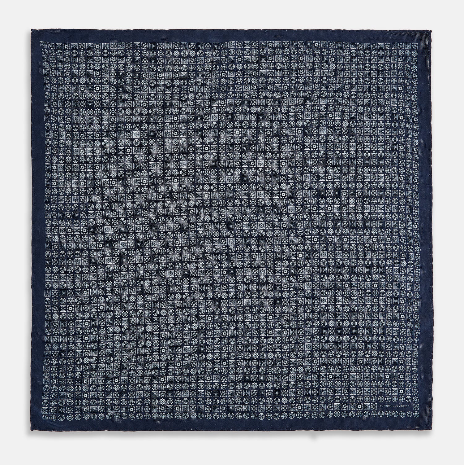 View 4 of product The Rosette Navy Pocket Square in Silk by Turnbull & Asser UK is a square, navy blue accessory featuring a small geometric pattern. Shown laid flat with one corner folded, it reveals a contrasting, finer motif on the reverse side. This elegant double-sided design offers versatile styling options for any occasion.
