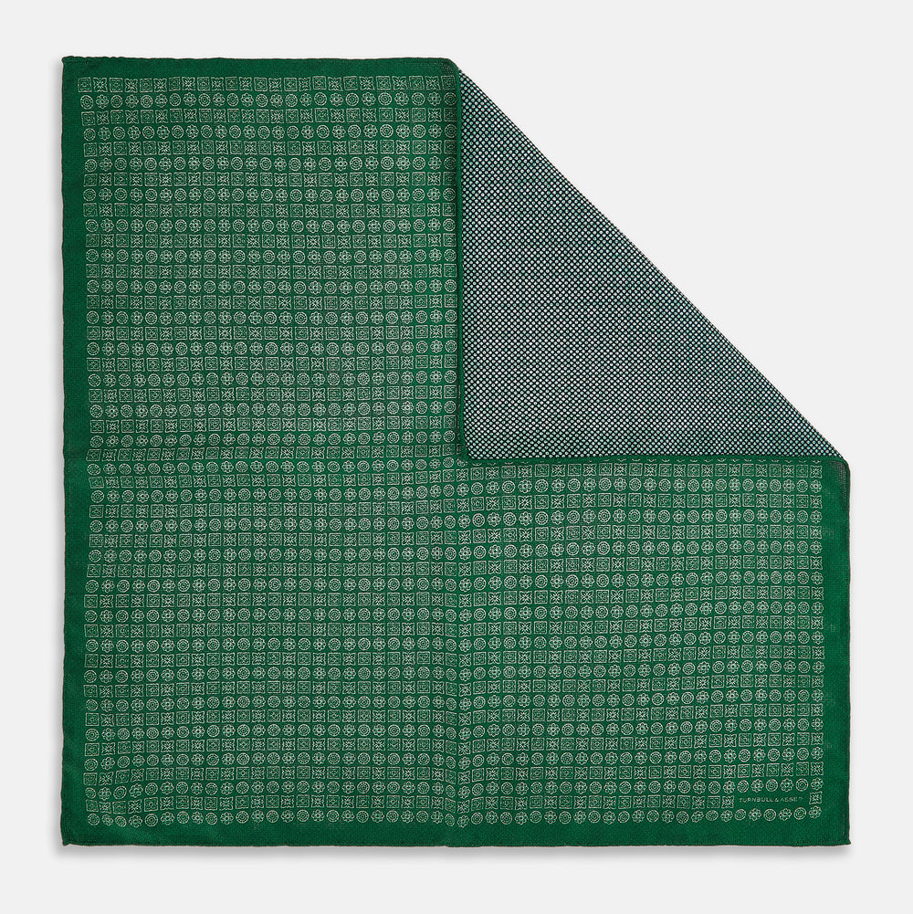 The Rosette Green Pocket Square in Silk by Turnbull & Asser UK features a small geometric medallion pattern and is shown folded to display a contrasting fine black-and-white design on the reverse side.