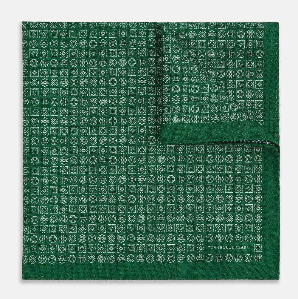 The Rosette Green Pocket Square in Silk by Turnbull & Asser UK features a small geometric medallion pattern and is shown folded to display a contrasting fine black-and-white design on the reverse side.