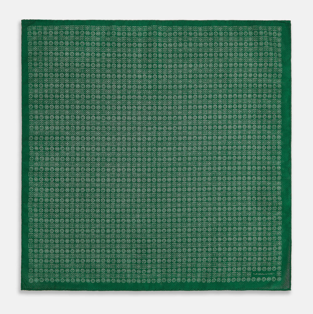 The Rosette Green Pocket Square in Silk by Turnbull & Asser UK features a small geometric medallion pattern and is shown folded to display a contrasting fine black-and-white design on the reverse side.