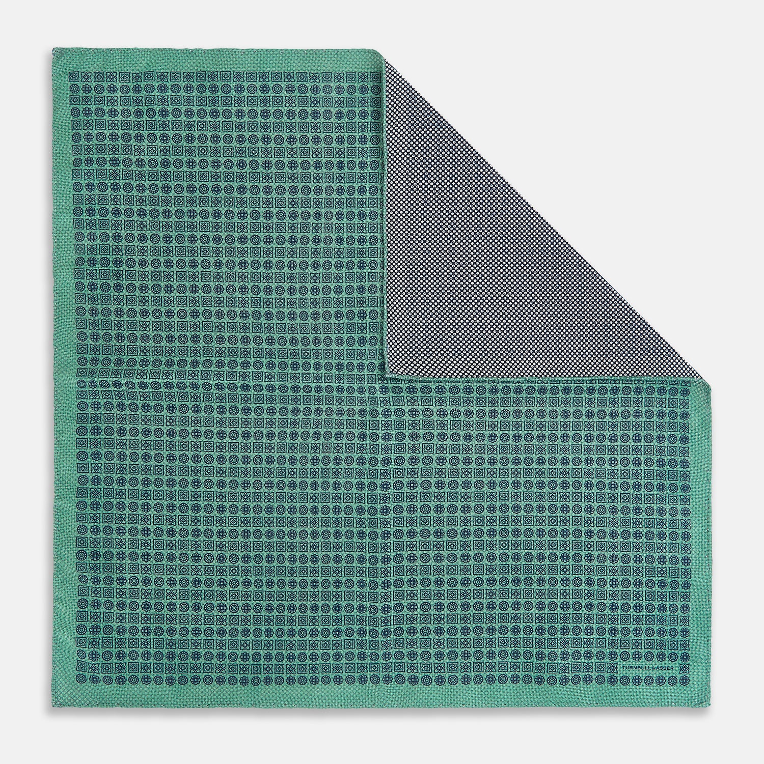 View 1 of product A square silk pocket square in Rosette Green by Turnbull & Asser UK, featuring a teal base with a grid of dark dots. One corner is folded to showcase the black and white microdot pattern on the reverse, while subtle hints of navy, aqua, and green form geometric medallions that lend a refined modern touch.
