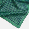 View 3 of product A square silk pocket square in Rosette Green by Turnbull & Asser UK, featuring a teal base with a grid of dark dots. One corner is folded to showcase the black and white microdot pattern on the reverse, while subtle hints of navy, aqua, and green form geometric medallions that lend a refined modern touch.