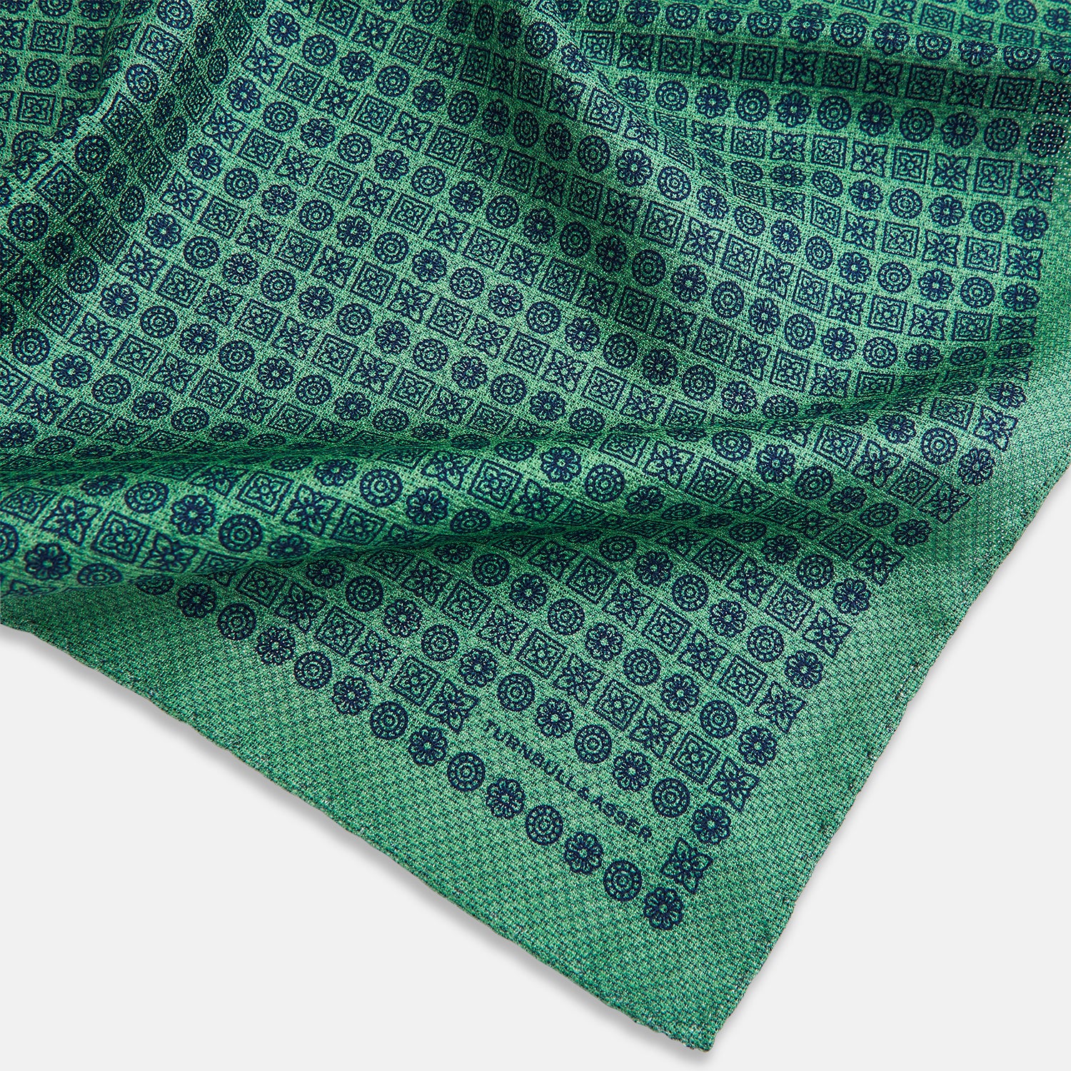 View 3 of product A square silk pocket square in Rosette Green by Turnbull & Asser UK, featuring a teal base with a grid of dark dots. One corner is folded to showcase the black and white microdot pattern on the reverse, while subtle hints of navy, aqua, and green form geometric medallions that lend a refined modern touch.
