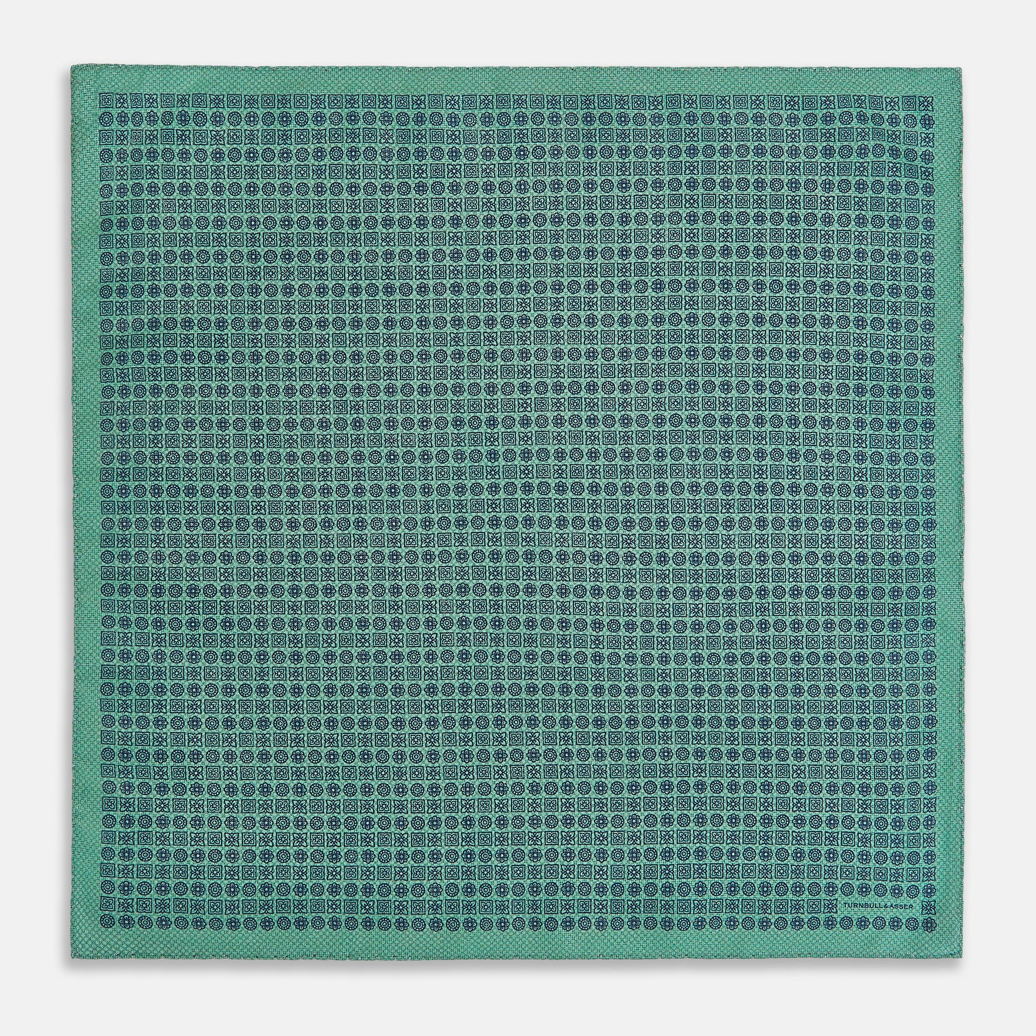 View 5 of product A square silk pocket square in Rosette Green by Turnbull & Asser UK, featuring a teal base with a grid of dark dots. One corner is folded to showcase the black and white microdot pattern on the reverse, while subtle hints of navy, aqua, and green form geometric medallions that lend a refined modern touch.