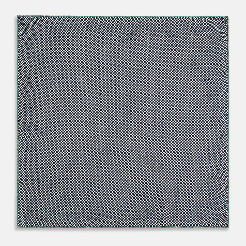 A square silk pocket square in Rosette Green by Turnbull & Asser UK, featuring a teal base with a grid of dark dots. One corner is folded to showcase the black and white microdot pattern on the reverse, while subtle hints of navy, aqua, and green form geometric medallions that lend a refined modern touch.