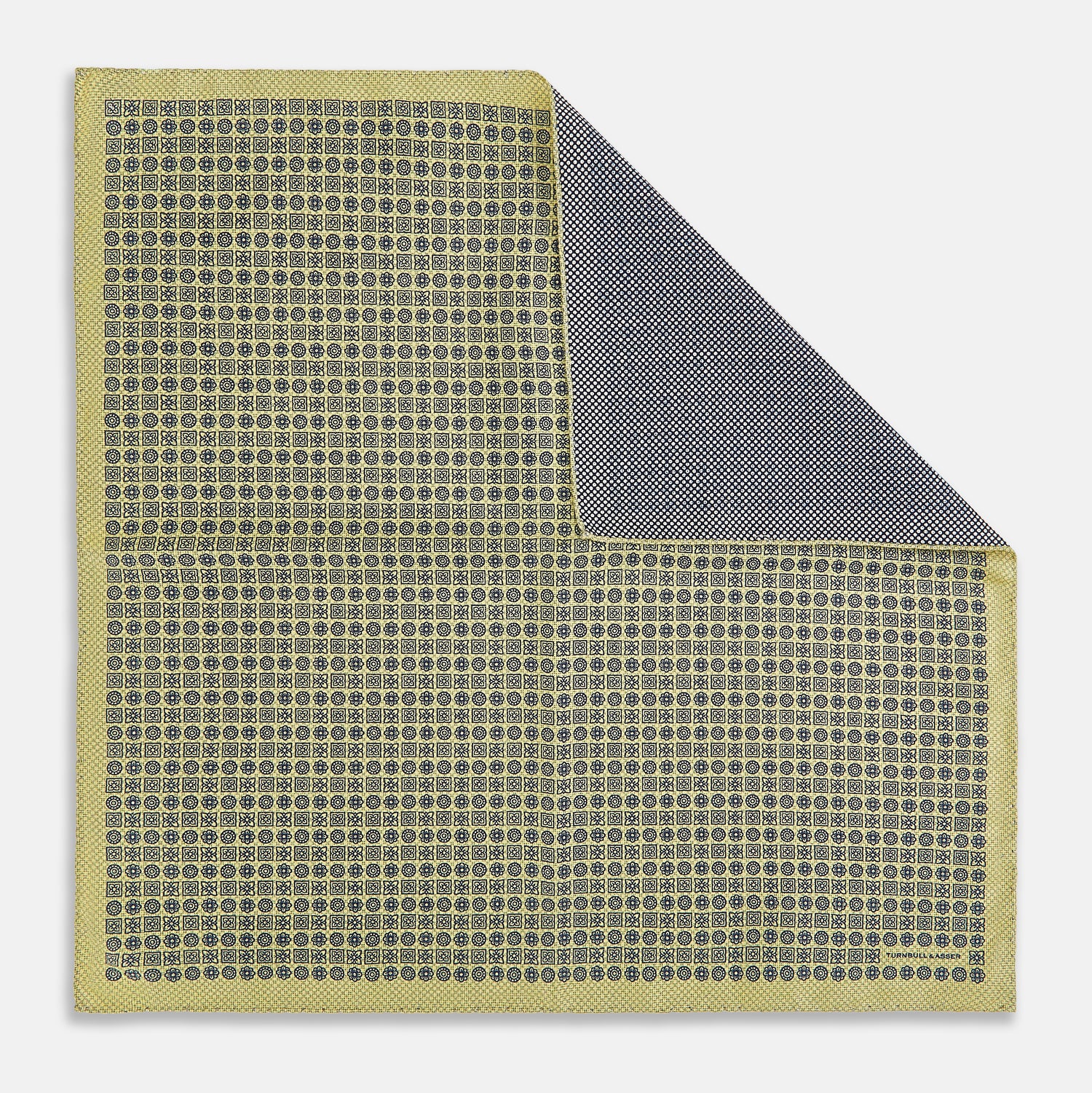 View 1 of product The Rosette Yellow Pocket Square in Silk by Turnbull & Asser UK features a square design with a yellow border, adorned with a grid of small black and white circles. One corner is neatly folded to reveal a reverse side in a refined black and white micro-checkered pattern, while subtle geometric medallions lend an added touch of elegance to the overall look.