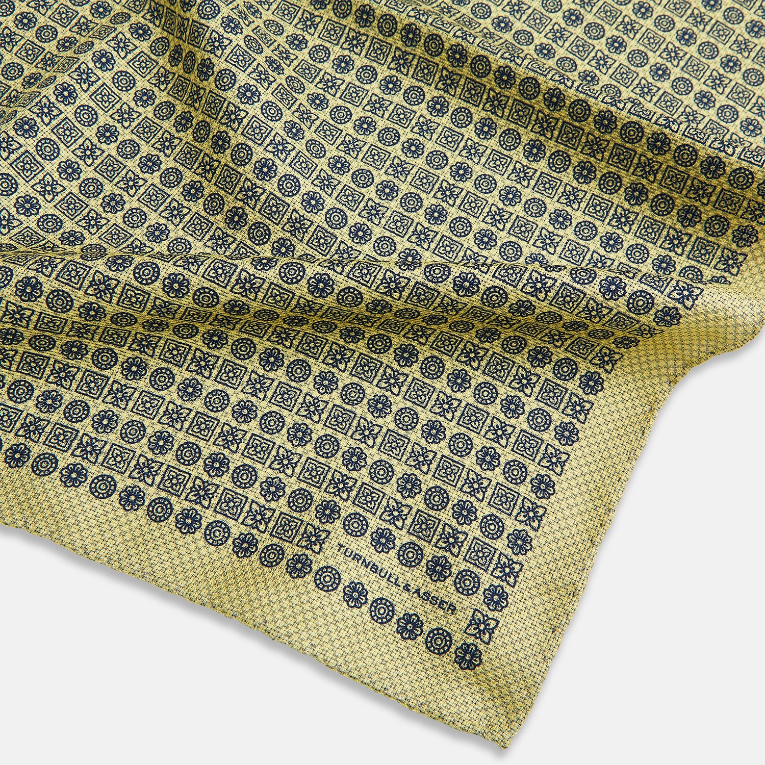 View 3 of product The Rosette Yellow Pocket Square in Silk by Turnbull & Asser UK features a square design with a yellow border, adorned with a grid of small black and white circles. One corner is neatly folded to reveal a reverse side in a refined black and white micro-checkered pattern, while subtle geometric medallions lend an added touch of elegance to the overall look.