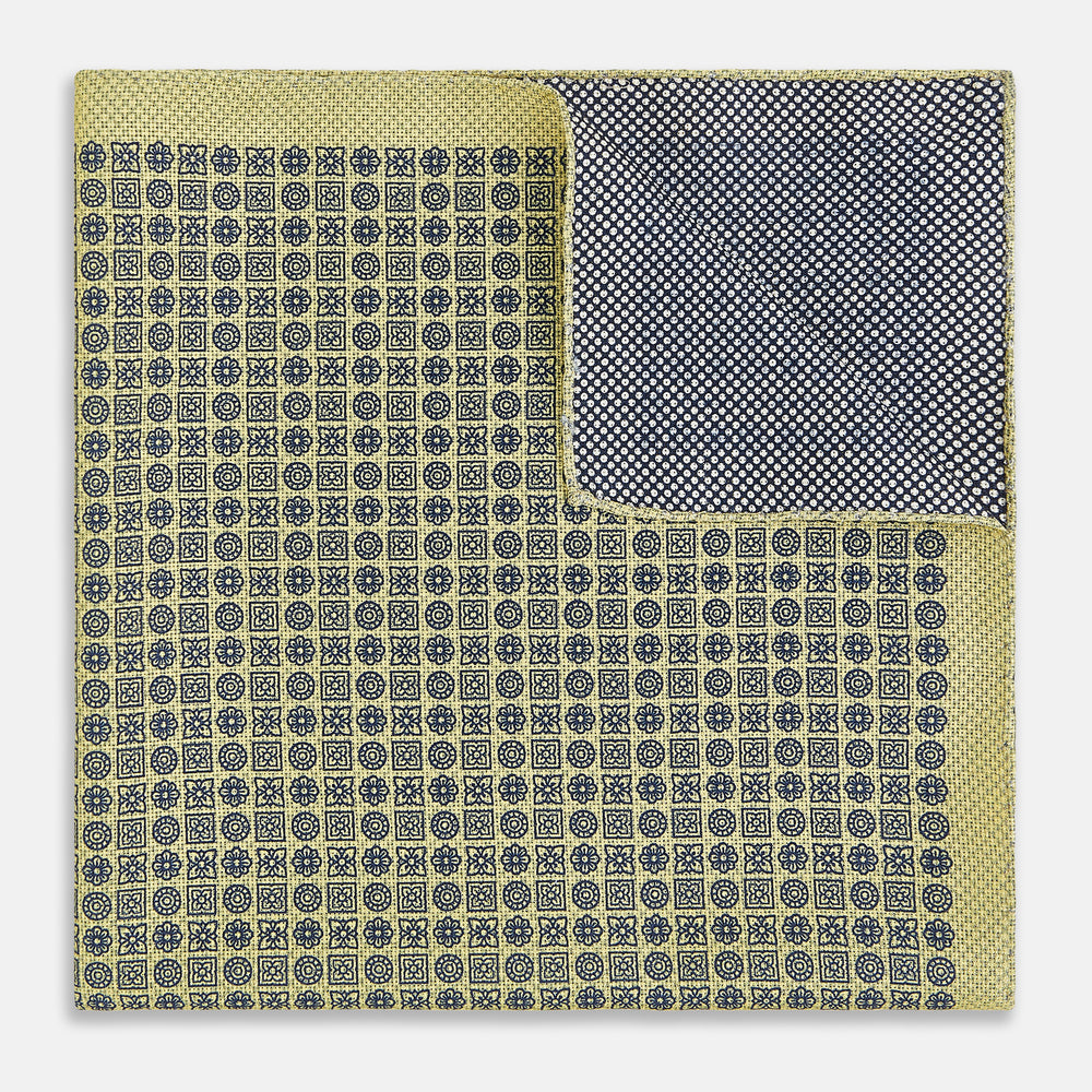 The Rosette Yellow Pocket Square in Silk by Turnbull & Asser UK features a square design with a yellow border, adorned with a grid of small black and white circles. One corner is neatly folded to reveal a reverse side in a refined black and white micro-checkered pattern, while subtle geometric medallions lend an added touch of elegance to the overall look.