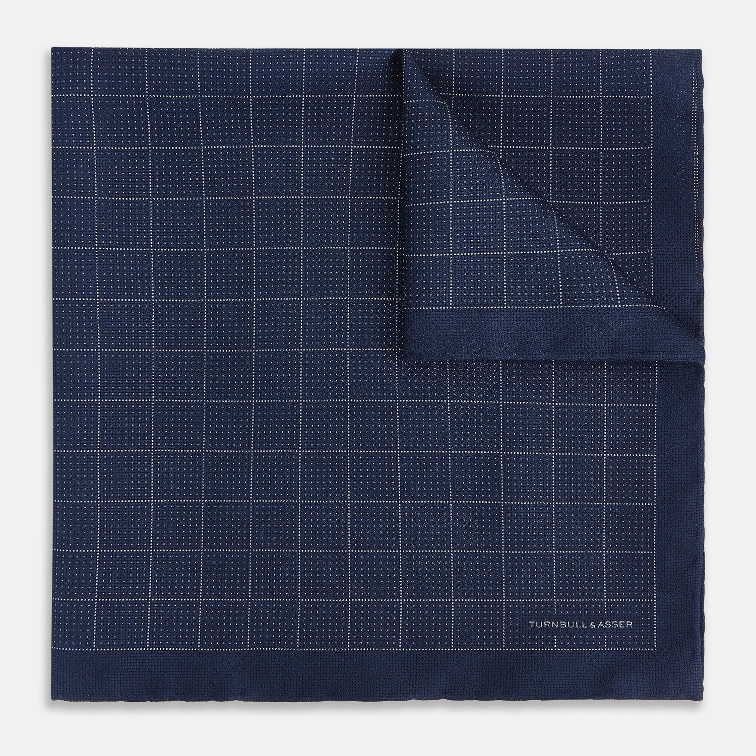 View 2 of product The Checked Blue Pocket Square in Silk by Turnbull & Asser UK features a navy base with a light blue grid pattern on one side and a refined dotted design on the other. This double-sided accessory is shown partially folded to elegantly showcase both distinctive patterns.
