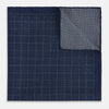 View 4 of product The Checked Blue Pocket Square in Silk by Turnbull & Asser UK features a navy base with a light blue grid pattern on one side and a refined dotted design on the other. This double-sided accessory is shown partially folded to elegantly showcase both distinctive patterns.