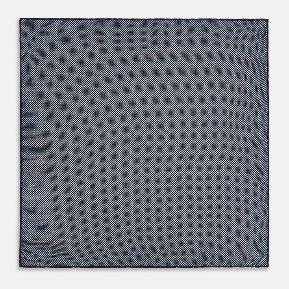The Checked Blue Pocket Square in Silk by Turnbull & Asser UK features a navy base with a light blue grid pattern on one side and a refined dotted design on the other. This double-sided accessory is shown partially folded to elegantly showcase both distinctive patterns.