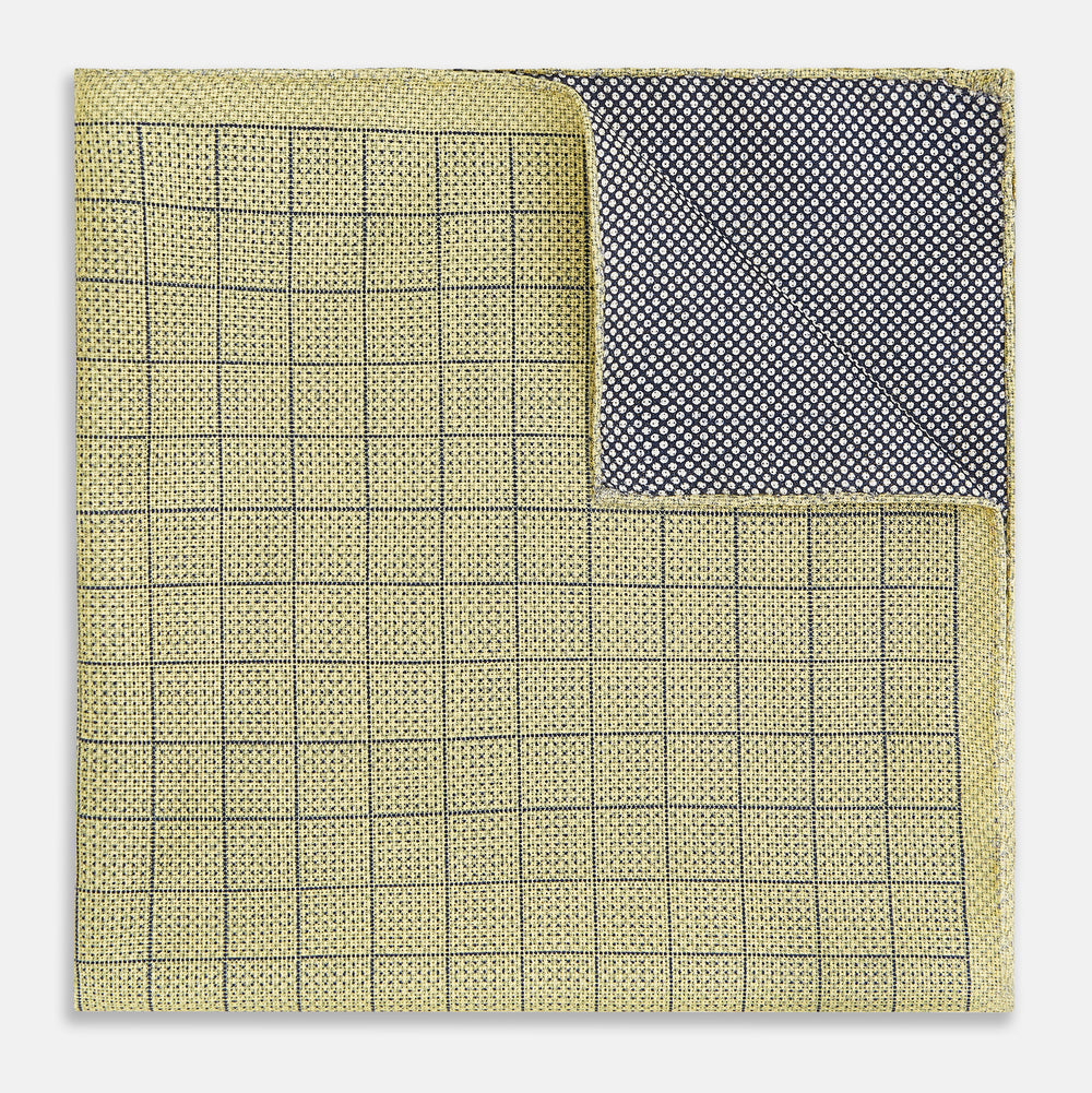 A yellow silk pocket square featuring a small black grid pattern of dotted squares, neatly folded at one corner. "Turnbull & Asser UK" is printed in the bottom right corner.