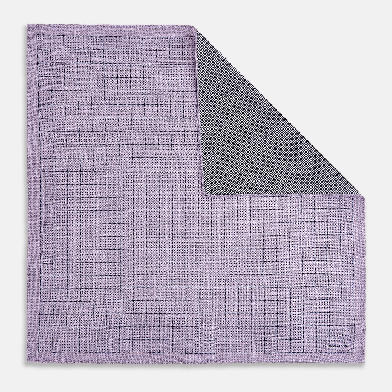 View 1 of product The Checked Lilac Pocket Square in Silk by Turnbull & Asser UK features a grid pattern in purple with a solid border, neatly folded to display its double-sided design and contrasting black and white dotted squares on the reverse side.