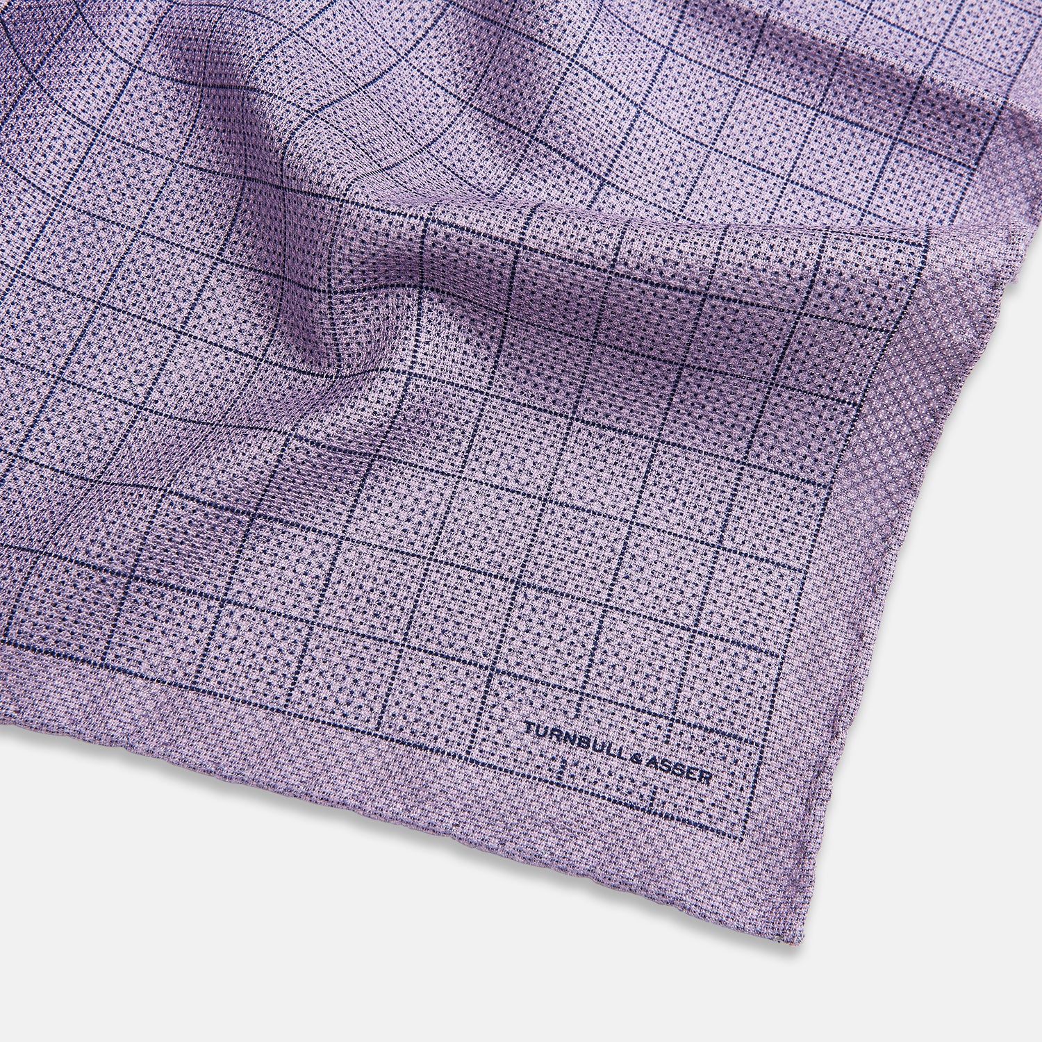 View 3 of product The Checked Lilac Pocket Square in Silk by Turnbull & Asser UK features a grid pattern in purple with a solid border, neatly folded to display its double-sided design and contrasting black and white dotted squares on the reverse side.