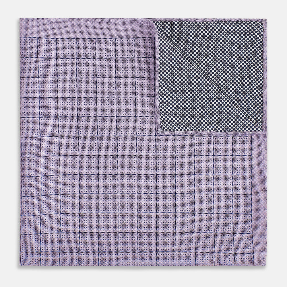 The Checked Lilac Pocket Square in Silk by Turnbull & Asser UK features a grid pattern in purple with a solid border, neatly folded to display its double-sided design and contrasting black and white dotted squares on the reverse side.