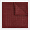 View 2 of product The Turnbull & Asser UK Checked Burgundy Pocket Square in Silk features a sophisticated burgundy hue with a subtle grid pattern. It's displayed folded at one corner to reveal a contrasting small checkered design on the reverse, showcasing its refined double-sided craftsmanship.