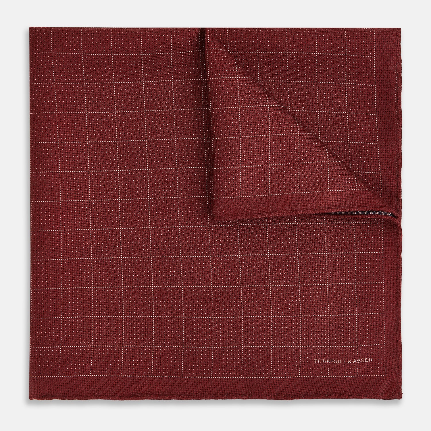 View 2 of product The Turnbull & Asser UK Checked Burgundy Pocket Square in Silk features a sophisticated burgundy hue with a subtle grid pattern. It's displayed folded at one corner to reveal a contrasting small checkered design on the reverse, showcasing its refined double-sided craftsmanship.