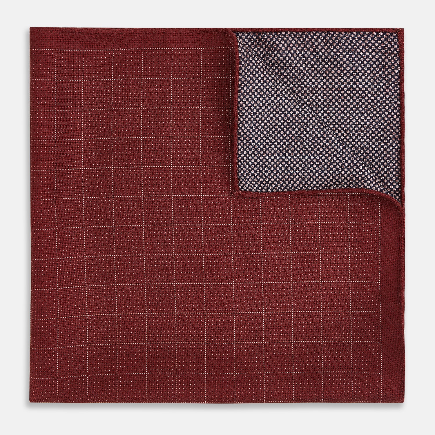 View 4 of product The Turnbull & Asser UK Checked Burgundy Pocket Square in Silk features a sophisticated burgundy hue with a subtle grid pattern. It's displayed folded at one corner to reveal a contrasting small checkered design on the reverse, showcasing its refined double-sided craftsmanship.