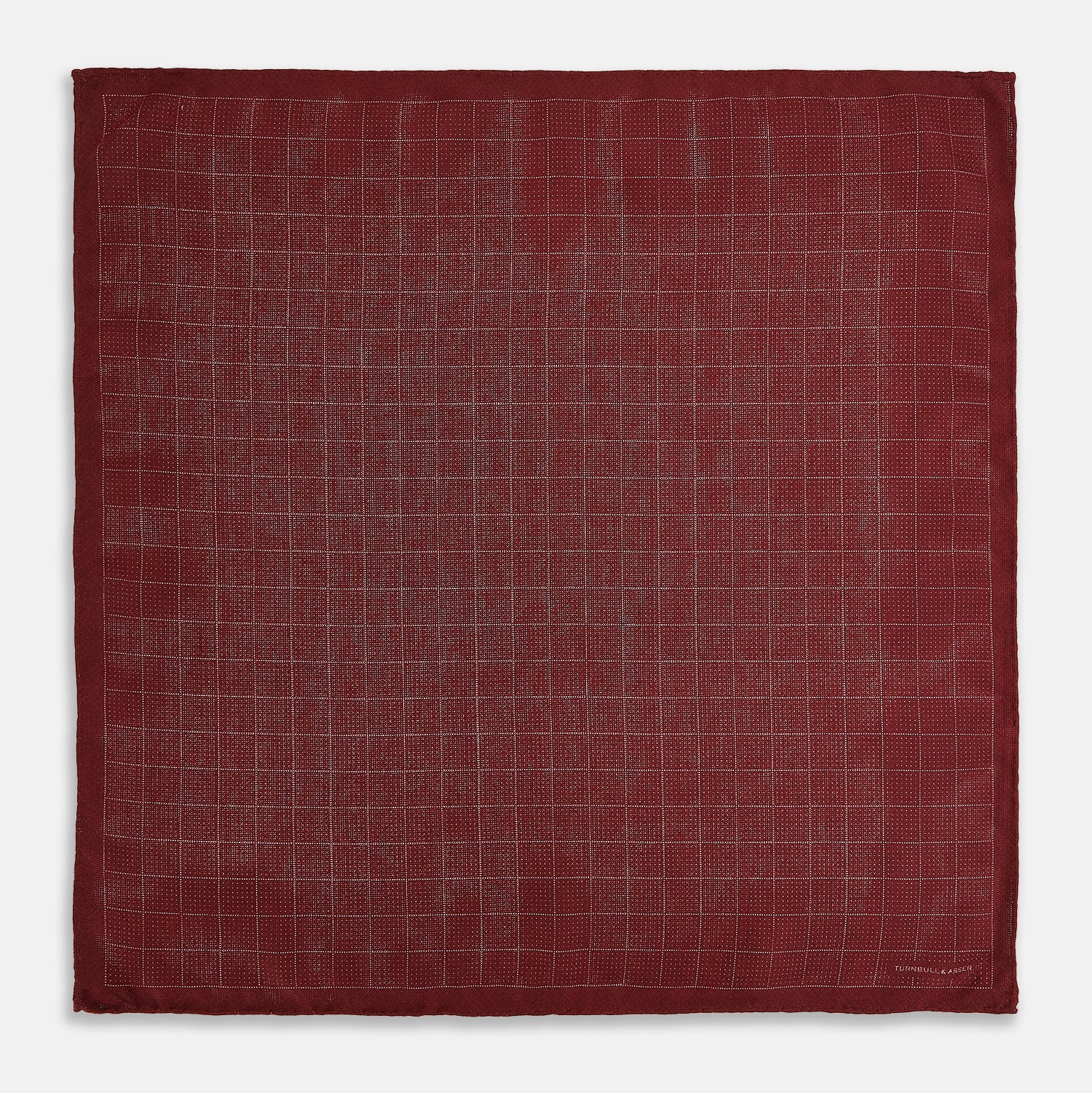 View 6 of product The Turnbull & Asser UK Checked Burgundy Pocket Square in Silk features a sophisticated burgundy hue with a subtle grid pattern. It's displayed folded at one corner to reveal a contrasting small checkered design on the reverse, showcasing its refined double-sided craftsmanship.