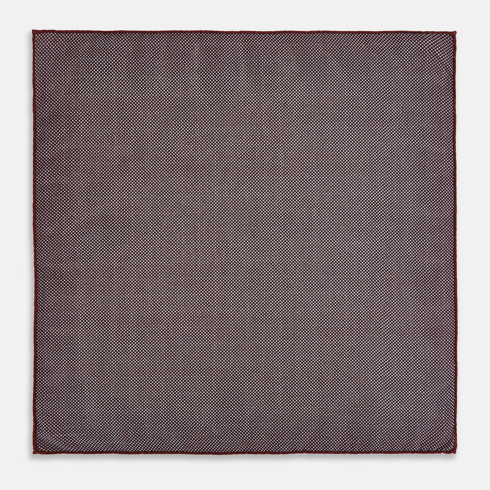 The Turnbull & Asser UK Checked Burgundy Pocket Square in Silk features a sophisticated burgundy hue with a subtle grid pattern. It's displayed folded at one corner to reveal a contrasting small checkered design on the reverse, showcasing its refined double-sided craftsmanship.