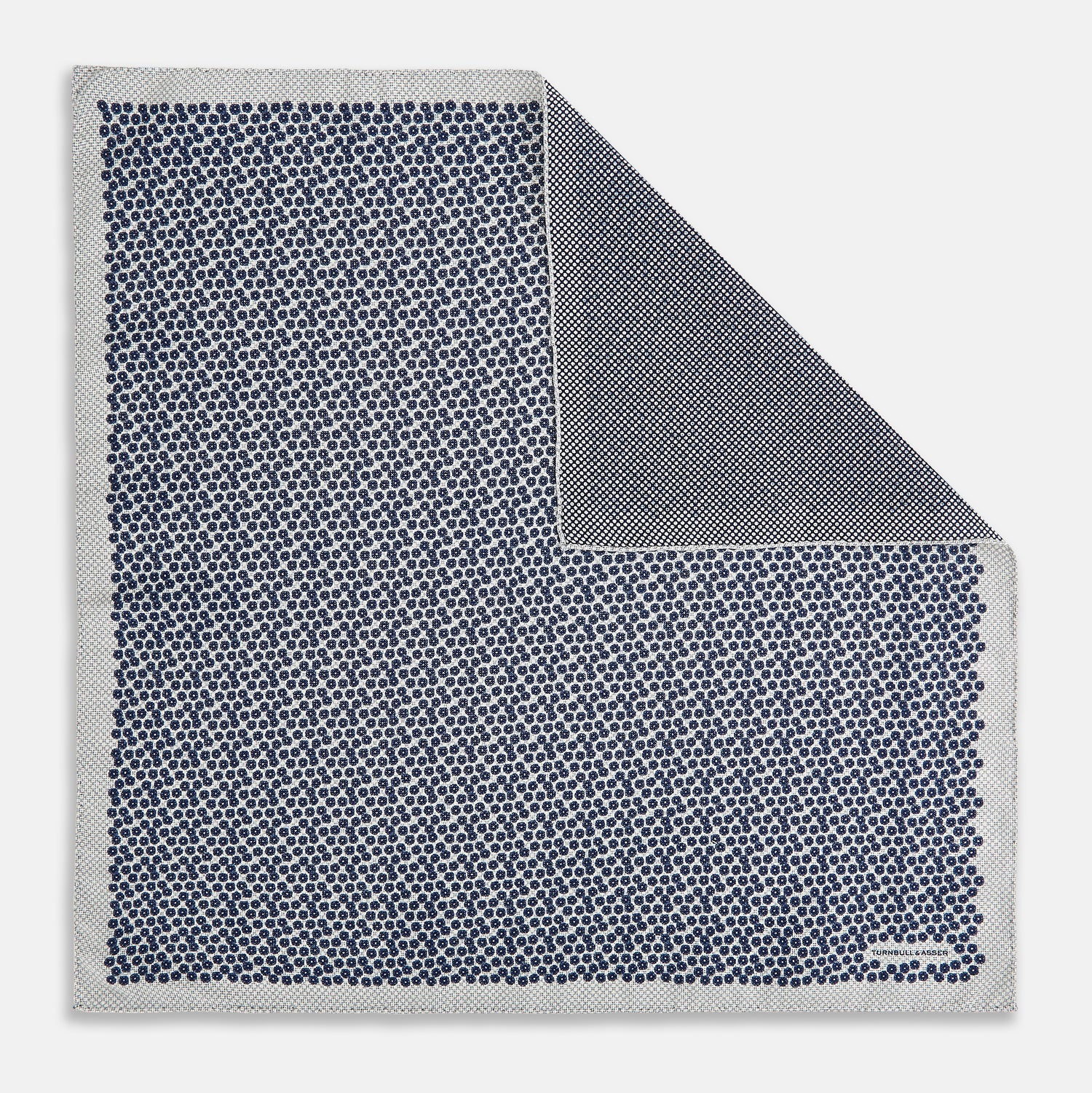 View 1 of product A square silk pocket square from Turnbull & Asser UK, featuring a subtle floral grey pattern; one corner is folded to reveal its double-sided design with a complementary pattern on the reverse side.