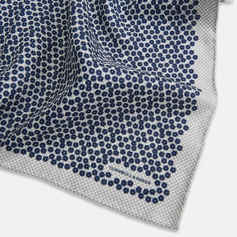 A square silk pocket square from Turnbull & Asser UK, featuring a subtle floral grey pattern; one corner is folded to reveal its double-sided design with a complementary pattern on the reverse side.