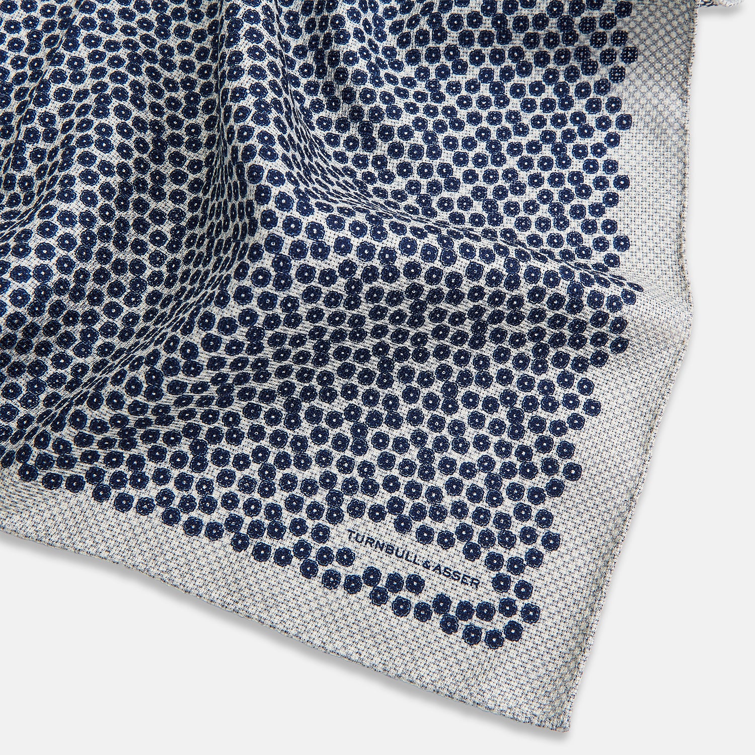 View 3 of product A square silk pocket square from Turnbull & Asser UK, featuring a subtle floral grey pattern; one corner is folded to reveal its double-sided design with a complementary pattern on the reverse side.