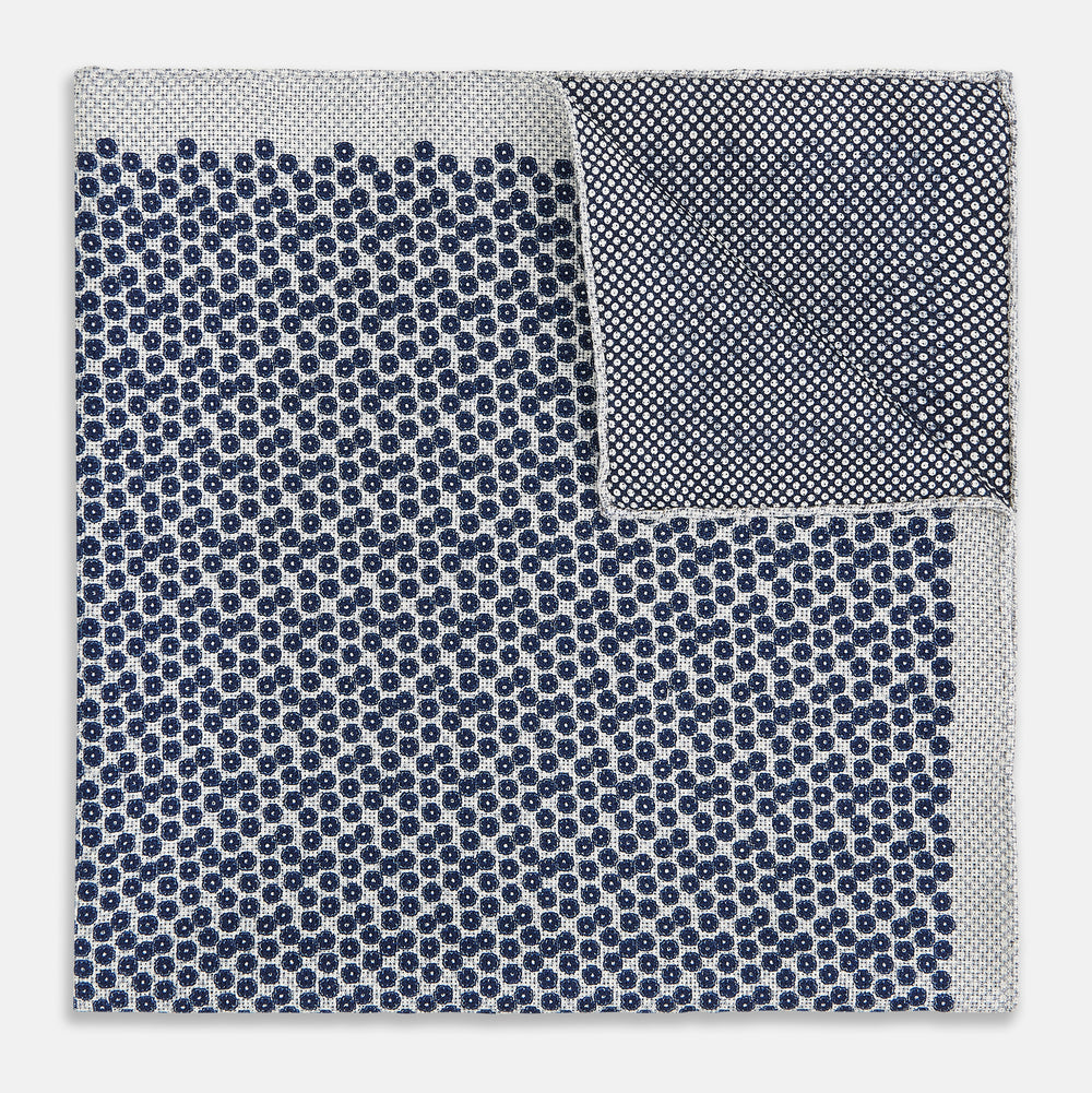 A square silk pocket square from Turnbull & Asser UK, featuring a subtle floral grey pattern; one corner is folded to reveal its double-sided design with a complementary pattern on the reverse side.
