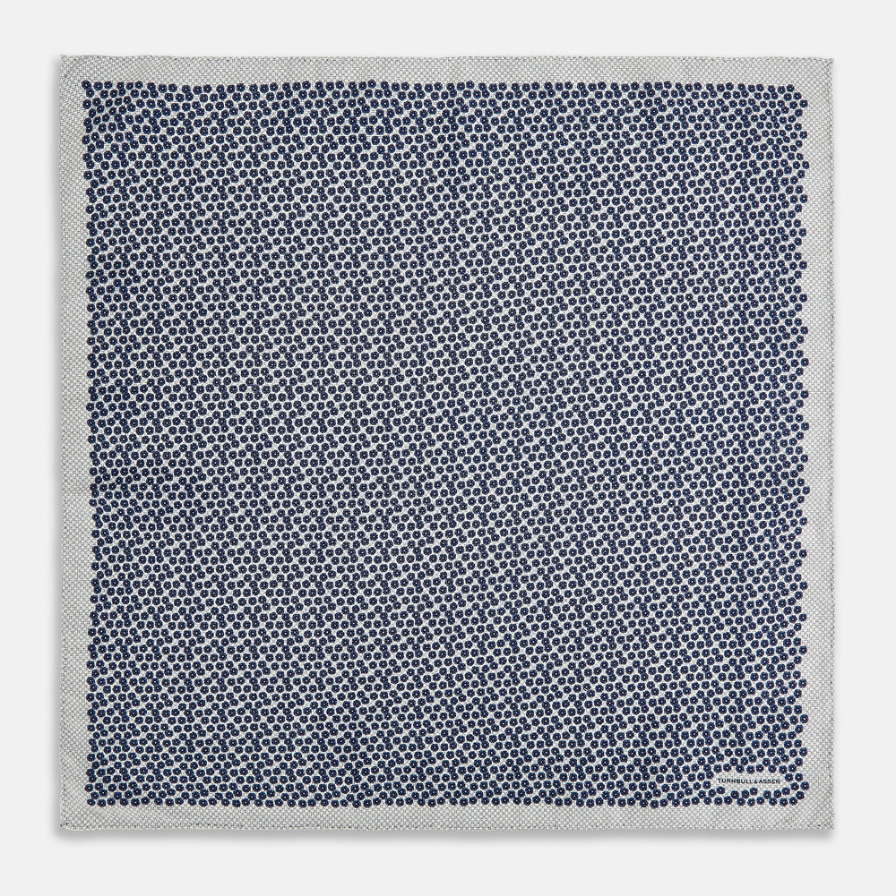 A square silk pocket square from Turnbull & Asser UK, featuring a subtle floral grey pattern; one corner is folded to reveal its double-sided design with a complementary pattern on the reverse side.