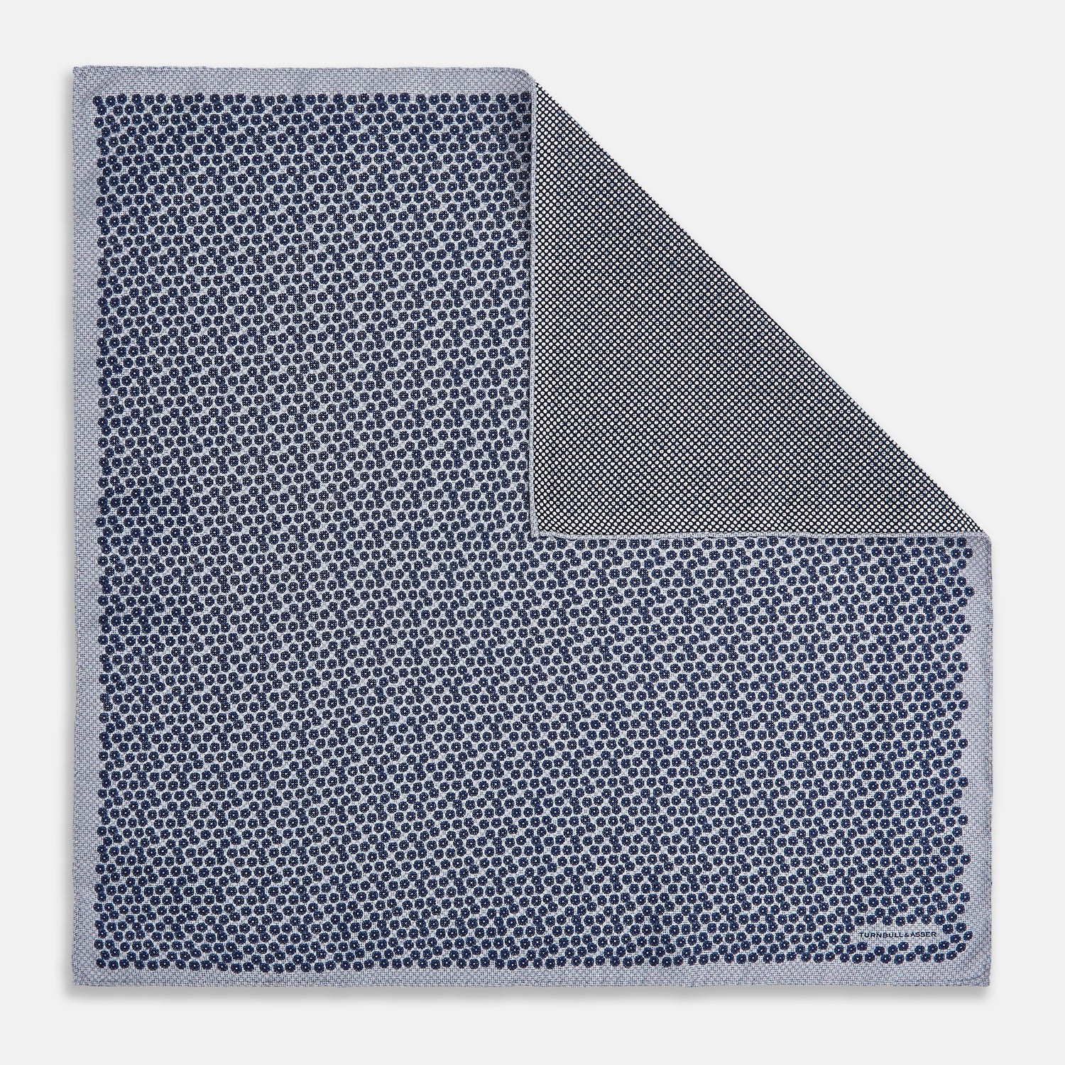 View 1 of product The Turnbull & Asser UK Floral Blue Pocket Square in Silk showcases a refined double-sided design, with a clustered dot pattern in blue and white on the front and a delicate fine dotted motif on the back. Presented with one corner elegantly folded, it exudes sophisticated style.