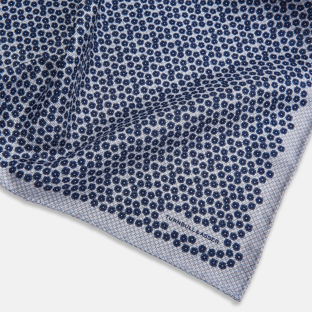 The Turnbull & Asser UK Floral Blue Pocket Square in Silk showcases a refined double-sided design, with a clustered dot pattern in blue and white on the front and a delicate fine dotted motif on the back. Presented with one corner elegantly folded, it exudes sophisticated style.