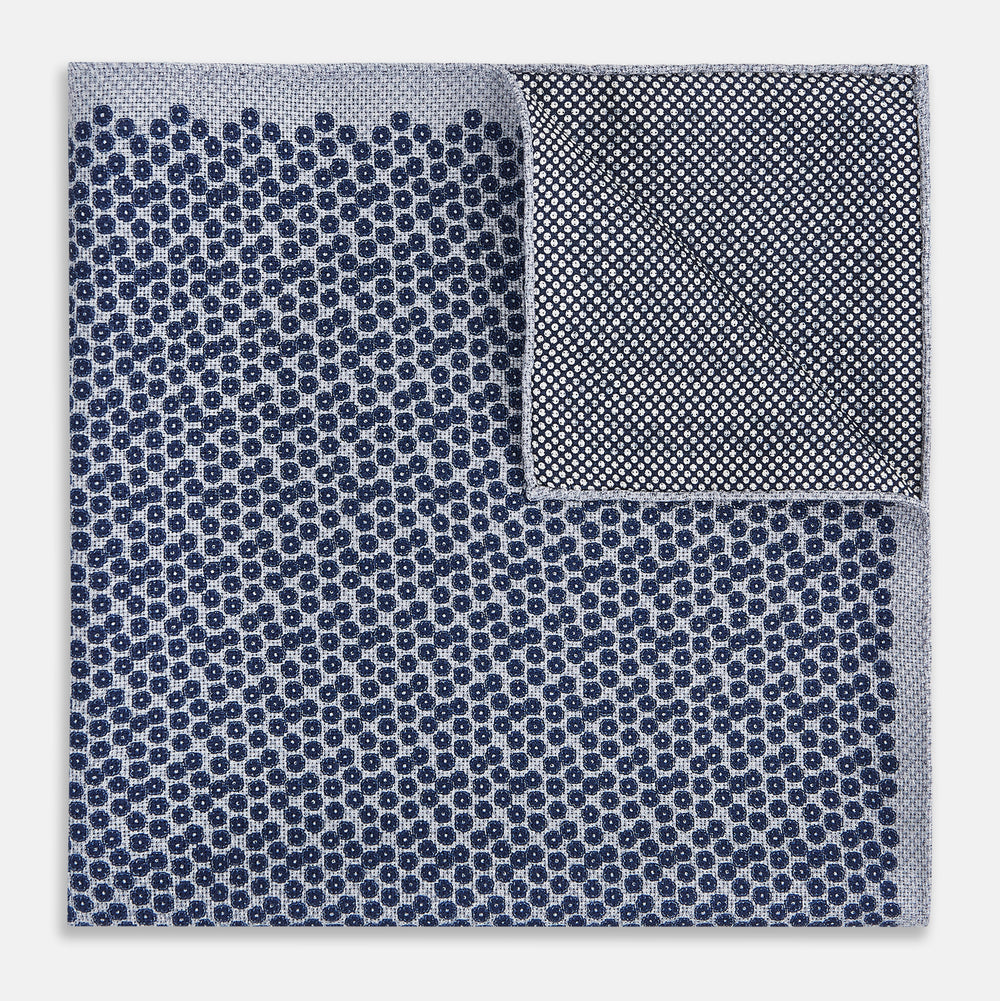 The Turnbull & Asser UK Floral Blue Pocket Square in Silk showcases a refined double-sided design, with a clustered dot pattern in blue and white on the front and a delicate fine dotted motif on the back. Presented with one corner elegantly folded, it exudes sophisticated style.