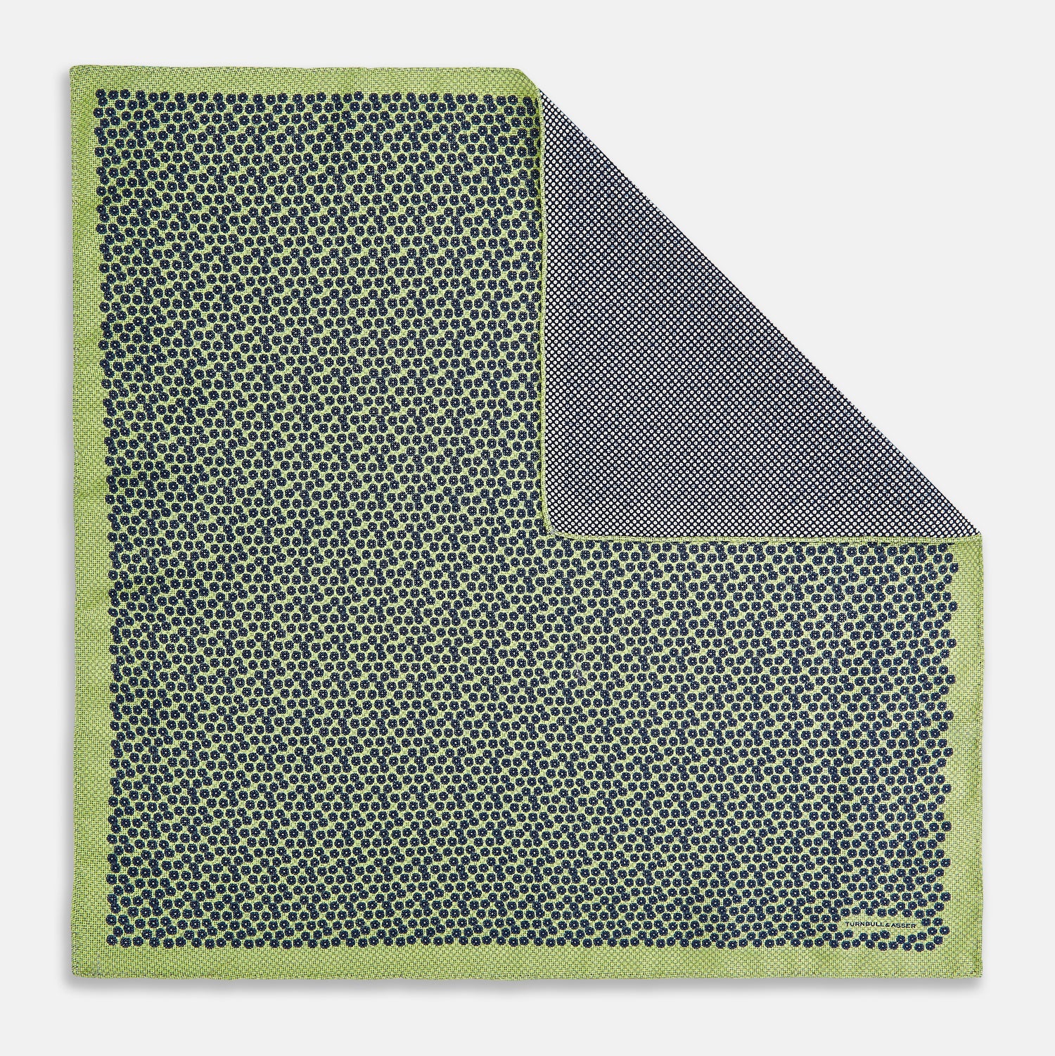 View 1 of product The Turnbull & Asser UK Floral Green Pocket Square in Silk is a square accessory featuring a blue floral pattern with a green border, partly folded at one corner to showcase its double-sided design, revealing a navy and light green dotted pattern on the reverse.