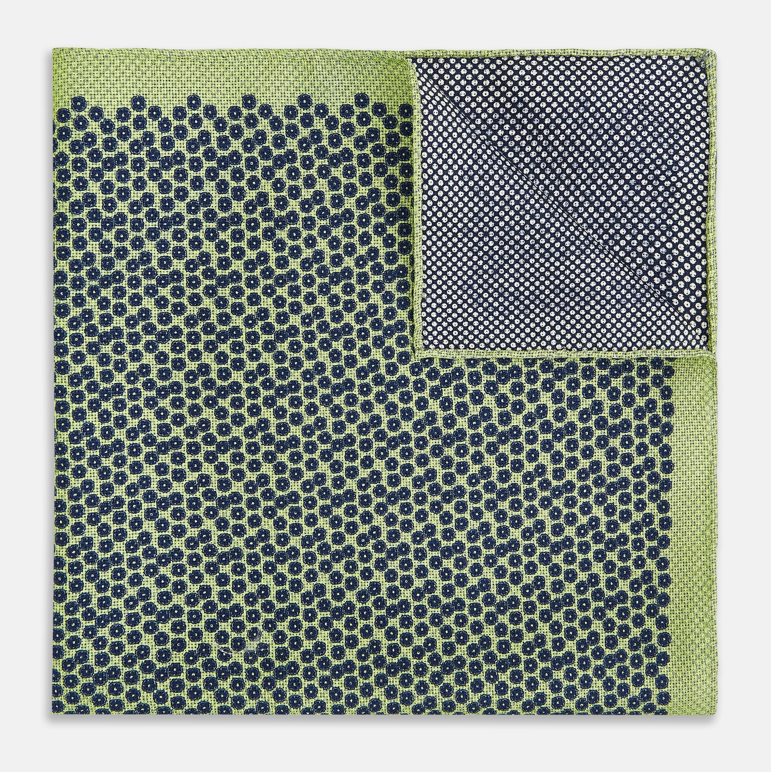 View 4 of product The Turnbull & Asser UK Floral Green Pocket Square in Silk is a square accessory featuring a blue floral pattern with a green border, partly folded at one corner to showcase its double-sided design, revealing a navy and light green dotted pattern on the reverse.