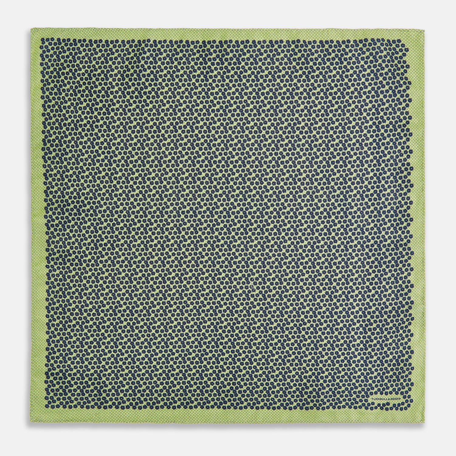 View 5 of product The Turnbull & Asser UK Floral Green Pocket Square in Silk is a square accessory featuring a blue floral pattern with a green border, partly folded at one corner to showcase its double-sided design, revealing a navy and light green dotted pattern on the reverse.