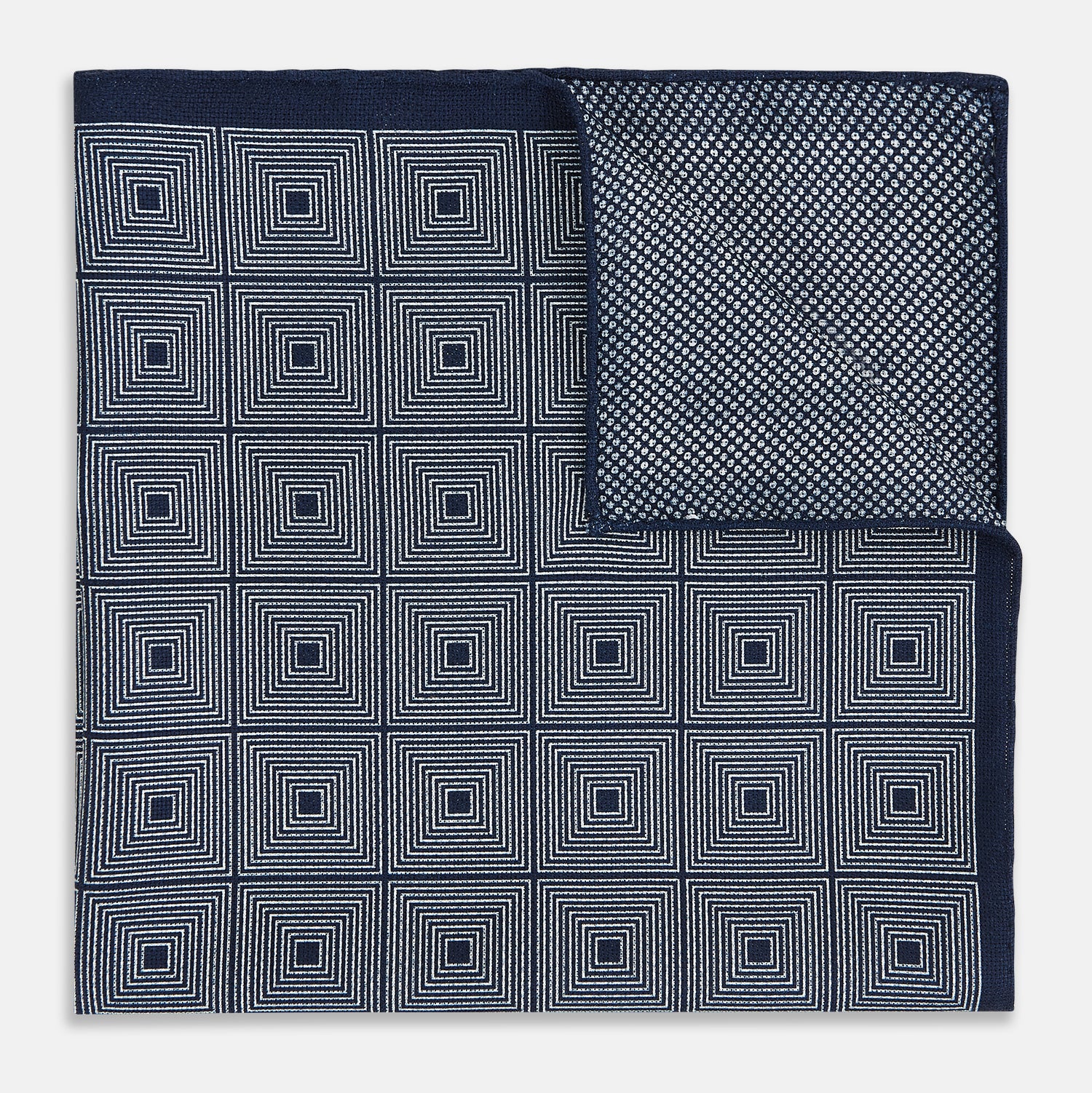 View 4 of product Introducing the Geometric Navy Tile Pocket Square in Silk by Turnbull & Asser UK—a folded navy and white accessory showcasing a double-sided design, with one side featuring concentric squares that form a striking geometric pattern and the other adorned with an elegant small dot motif.