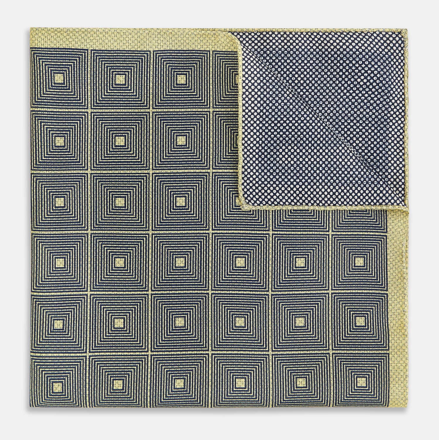View 4 of product The Turnbull & Asser UK Geometric Yellow Tile Pocket Square in Silk features a sophisticated geometric square pattern in gold and navy, accented with subtle concentric squares and a discreet label stitched into the bottom right corner. Its double-sided design is highlighted by a folded corner that reveals a contrasting dotted navy and white underside.