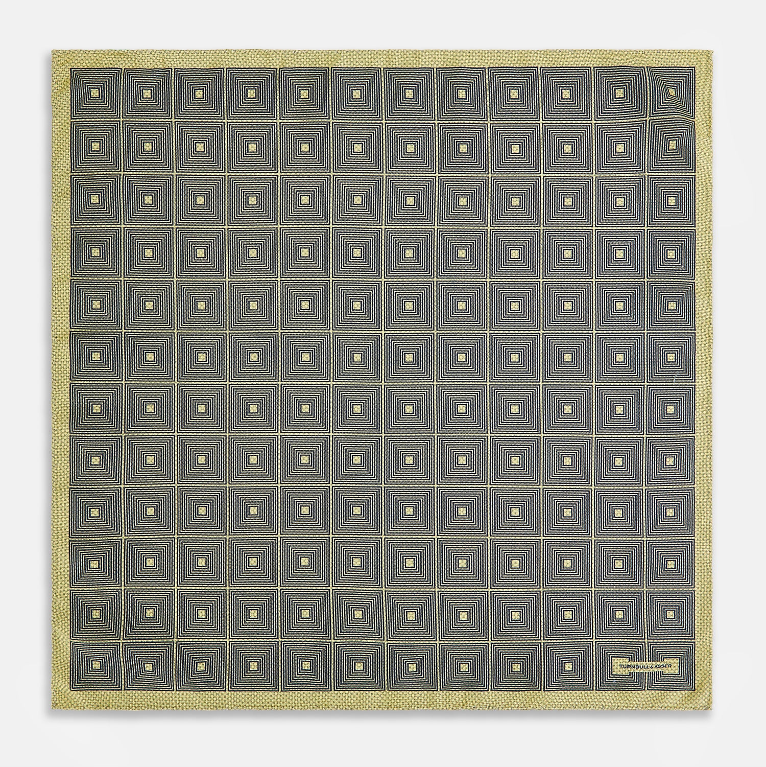View 5 of product The Turnbull & Asser UK Geometric Yellow Tile Pocket Square in Silk features a sophisticated geometric square pattern in gold and navy, accented with subtle concentric squares and a discreet label stitched into the bottom right corner. Its double-sided design is highlighted by a folded corner that reveals a contrasting dotted navy and white underside.
