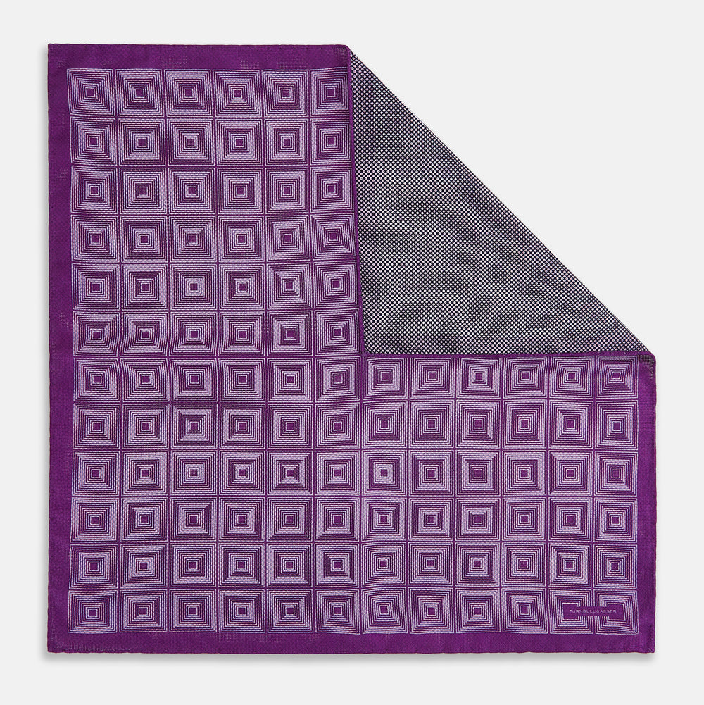 The Turnbull & Asser UK Geometric Purple Tile Pocket Square in Silk features a vibrant purple hue adorned with concentric square motifs. One corner is folded to reveal its double-sided design, showcasing a contrasting black-and-white dotted underside.