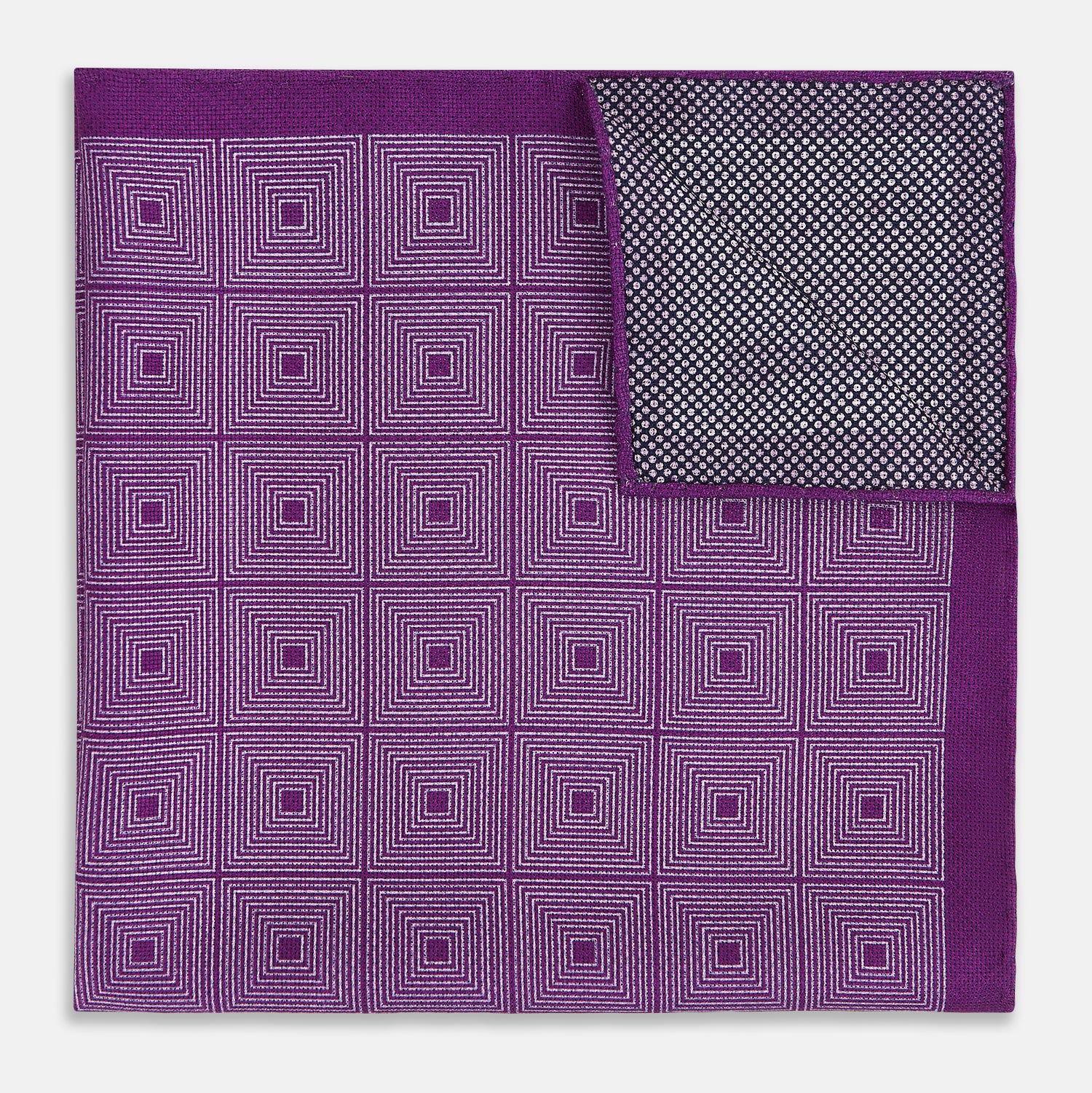 View 4 of product The Turnbull & Asser UK Geometric Purple Tile Pocket Square in Silk features a vibrant purple hue adorned with concentric square motifs. One corner is folded to reveal its double-sided design, showcasing a contrasting black-and-white dotted underside.