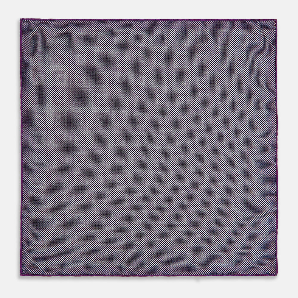 The Turnbull & Asser UK Geometric Purple Tile Pocket Square in Silk features a vibrant purple hue adorned with concentric square motifs. One corner is folded to reveal its double-sided design, showcasing a contrasting black-and-white dotted underside.