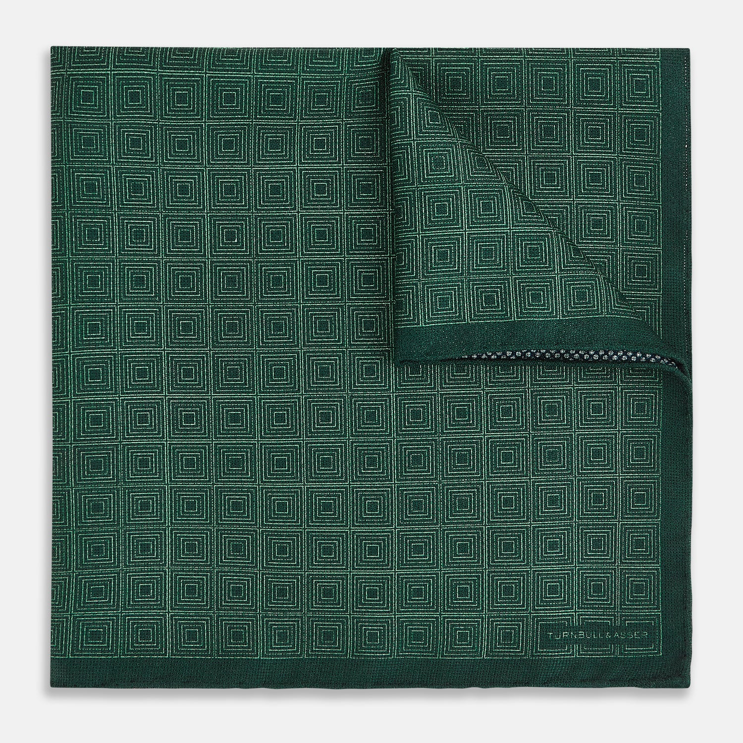 View 2 of product The Geometric Green Tile Pocket Square in Silk by Turnbull & Asser UK features a sophisticated tonal green design with a subtle pattern of concentric squares. One corner is folded to highlight the elegant double-sided construction, revealing a contrasting black and white small dot pattern on the reverse.