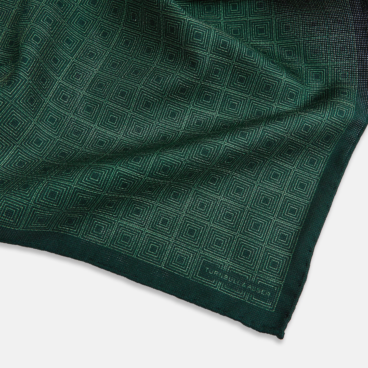 View 3 of product The Geometric Green Tile Pocket Square in Silk by Turnbull & Asser UK features a sophisticated tonal green design with a subtle pattern of concentric squares. One corner is folded to highlight the elegant double-sided construction, revealing a contrasting black and white small dot pattern on the reverse.