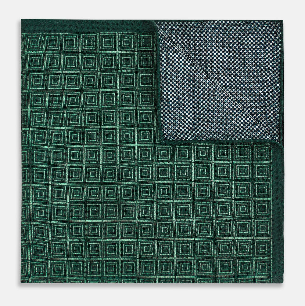 The Geometric Green Tile Pocket Square in Silk by Turnbull & Asser UK features a sophisticated tonal green design with a subtle pattern of concentric squares. One corner is folded to highlight the elegant double-sided construction, revealing a contrasting black and white small dot pattern on the reverse.