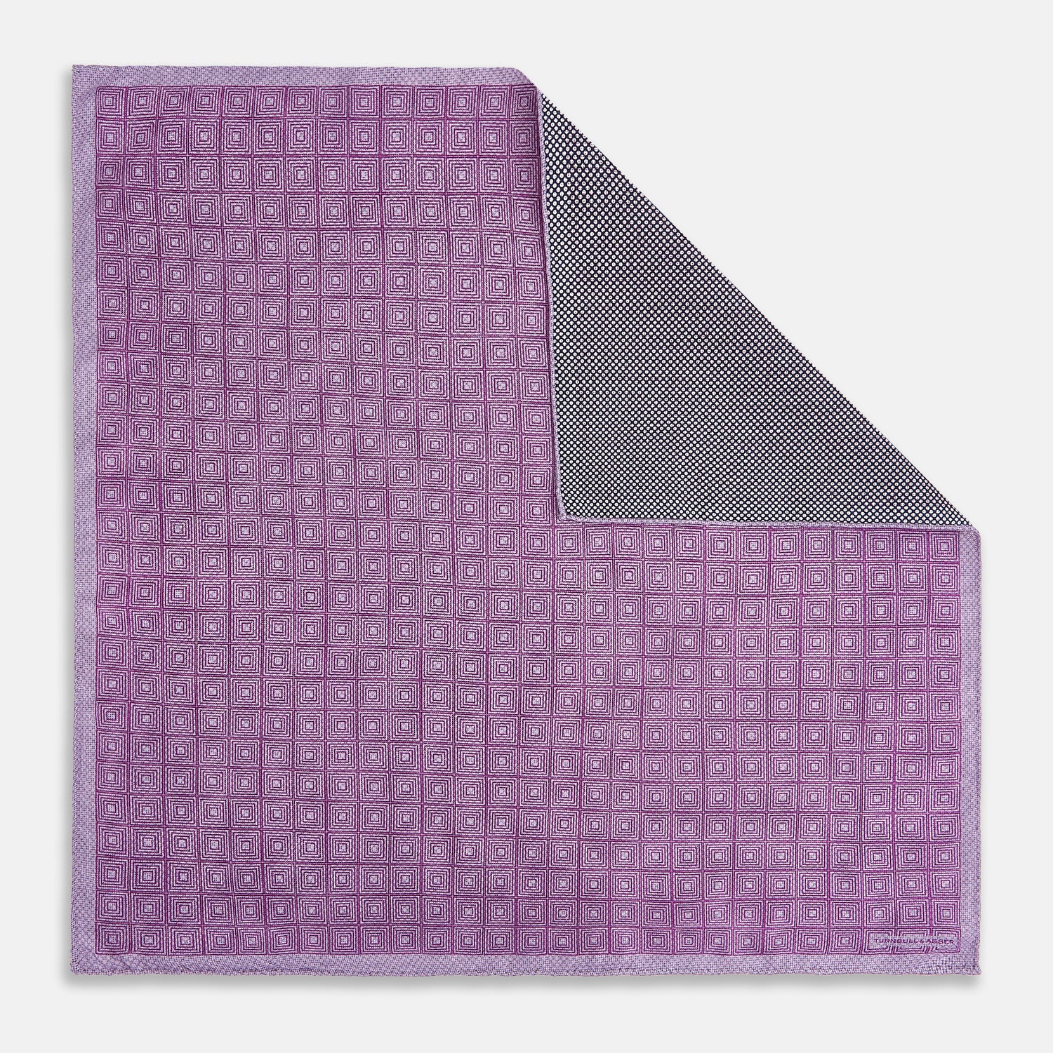 View 1 of product Certainly! Here’s a rewritten version of your sentence, incorporating the product data: The Geometric Lilac Tile Pocket Square in Silk by Turnbull & Asser UK features a lilac purple geometric pattern with a subtle square design, partially folded to reveal its double-sided construction with a contrasting black and white dotted pattern on the reverse.