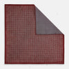 View 1 of product The Turnbull & Asser UK Geometric Burgundy Tile Pocket Square in Silk is displayed partly folded, showcasing its bold geometric grid pattern with concentric burgundy squares on the front and a contrasting black-and-white dotted design on the reverse.
