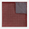 View 2 of product The Turnbull & Asser UK Geometric Burgundy Tile Pocket Square in Silk is displayed partly folded, showcasing its bold geometric grid pattern with concentric burgundy squares on the front and a contrasting black-and-white dotted design on the reverse.