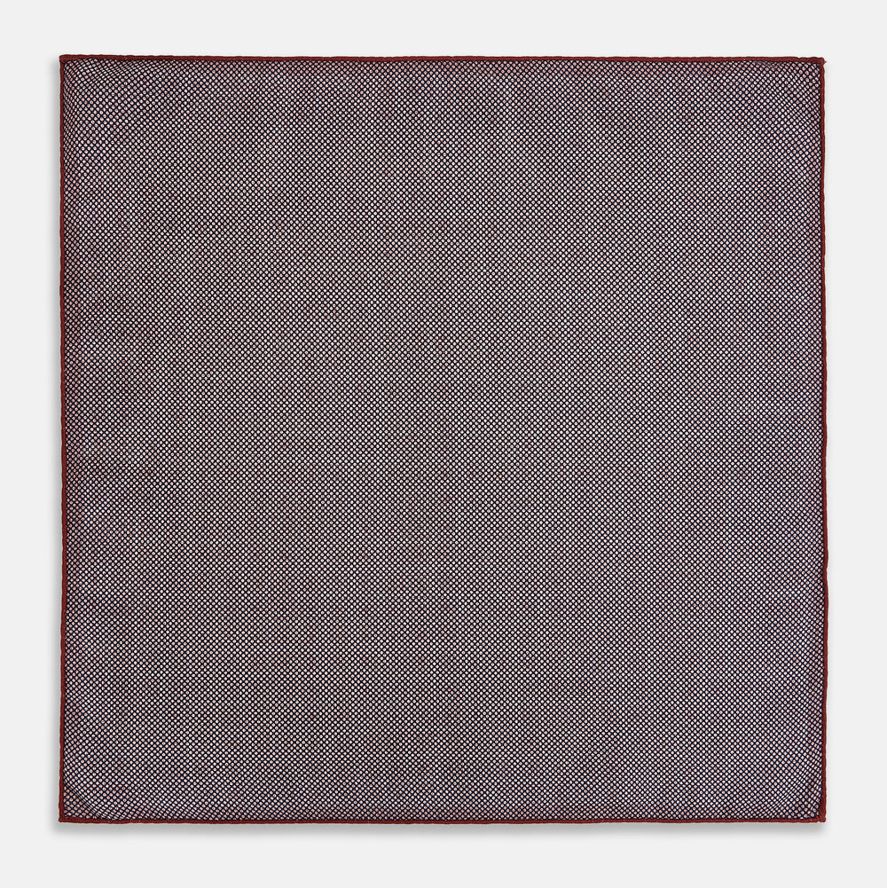 The Turnbull & Asser UK Geometric Burgundy Tile Pocket Square in Silk is displayed partly folded, showcasing its bold geometric grid pattern with concentric burgundy squares on the front and a contrasting black-and-white dotted design on the reverse.